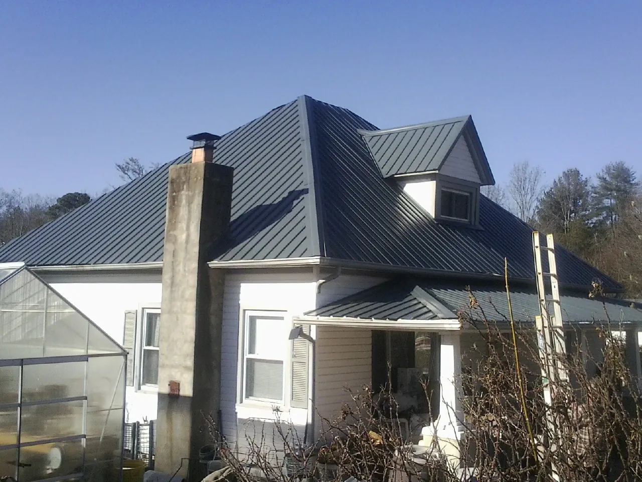 Dark blue standing seam metal roof on a white farmhouse with dormer — Slate & Tile Roof Repair by Roofing Brothers in Green Mountain