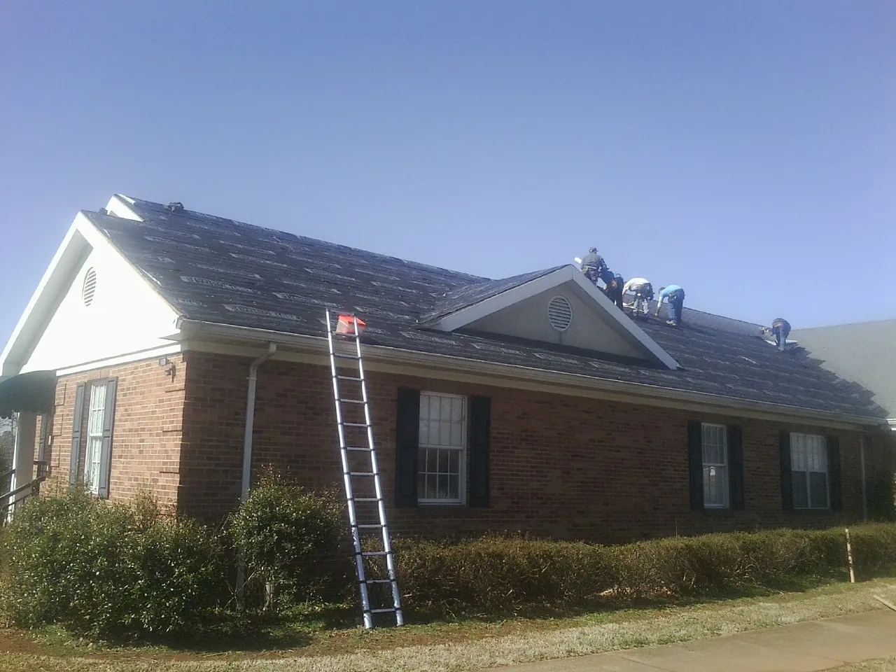 Crew tearing shingles off a brick ranch roof with a ladder set — Metal Roof Repair work by our crew in Green Mountain