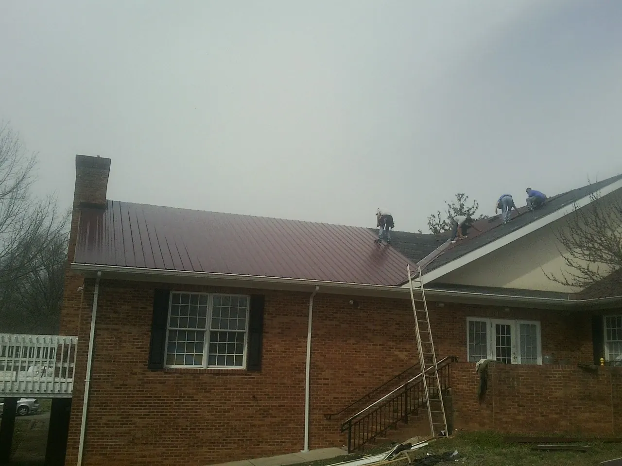 Crew setting red metal roofing panels on a brick home in Green Mountain
