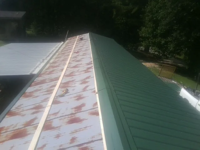 Old rusted panels beside newly installed green metal roofing — Wind Damage Roof Repair by Roofing Brothers in Green Mountain