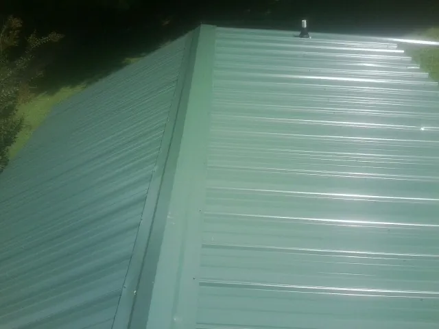 New green metal panels meeting at the ridge of a roof — Flat Roof Repair work by our crew in Green Mountain