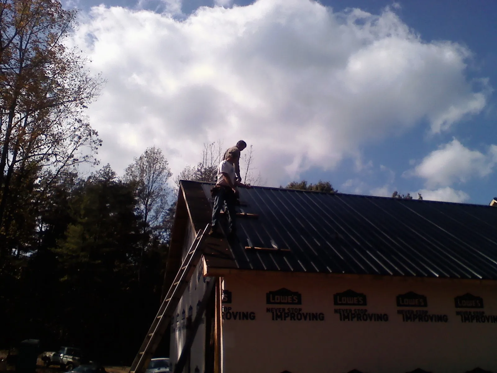 Roofer fastening dark metal panels high against a cloudy sky, from a Roof Inspection job in Green Mountain