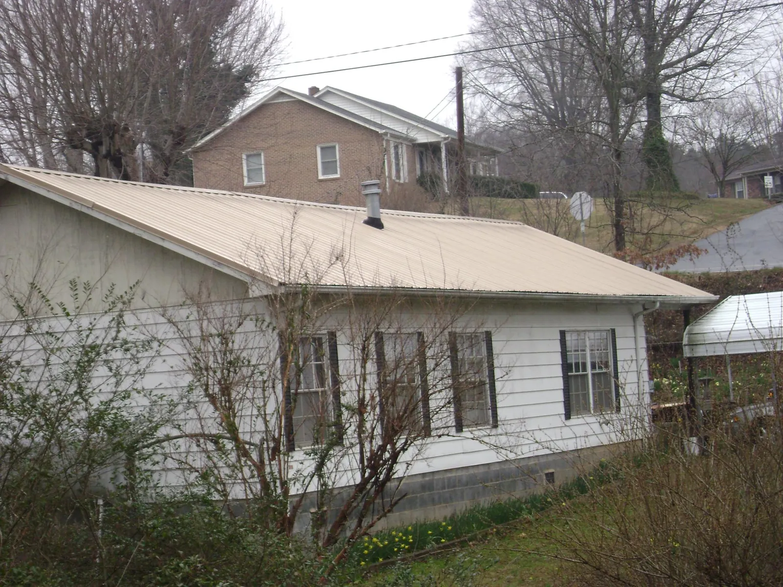Tan metal roof on a white sided house set into a hillside — Commercial Roofing by Roofing Brothers in Green Mountain