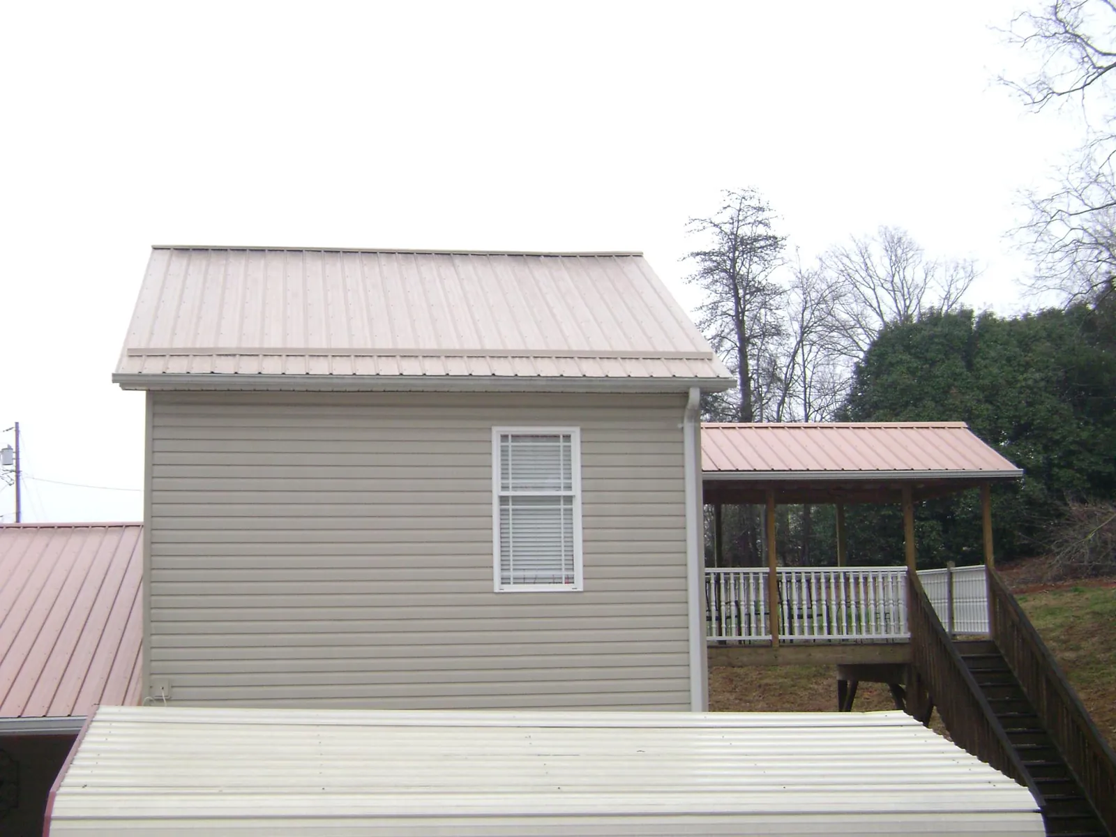 Tan metal roofs on a two story addition and attached porch, from a Roof Replacement job in Green Mountain
